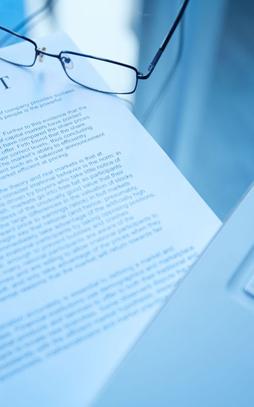 Image of document, eyeglasses and laptop on workplace